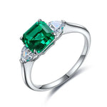 Load image into Gallery viewer, Silver ring featuring a square-cut emerald gemstone flanked by two smaller clear stones.
