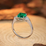 Load image into Gallery viewer, Silver ring featuring a square-cut emerald gemstone flanked by smaller diamonds.
