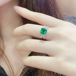 Load image into Gallery viewer, Emerald-cut green gemstone ring with diamond accents on a silver band.
