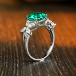 Load image into Gallery viewer, Elegant silver ring featuring a vibrant emerald-green gemstone centerpiece flanked by smaller clear diamonds.
