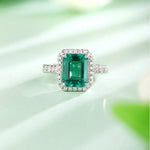 Load image into Gallery viewer, Emerald-cut green gemstone ring surrounded by small diamonds in a white metal setting.
