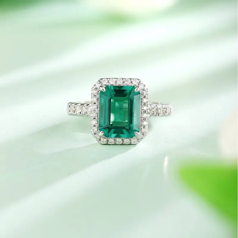 Emerald-cut green gemstone ring surrounded by small diamonds in a white metal setting.