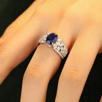 Load image into Gallery viewer, Ornate ring featuring a central oval blue gemstone surrounded by smaller white stones.
