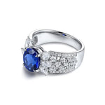 Load image into Gallery viewer, Silver ring featuring a prominent oval blue sapphire surrounded by small diamonds.
