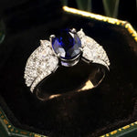 Load image into Gallery viewer, Elegant ring featuring a deep blue sapphire center stone flanked by diamond-encrusted bands.
