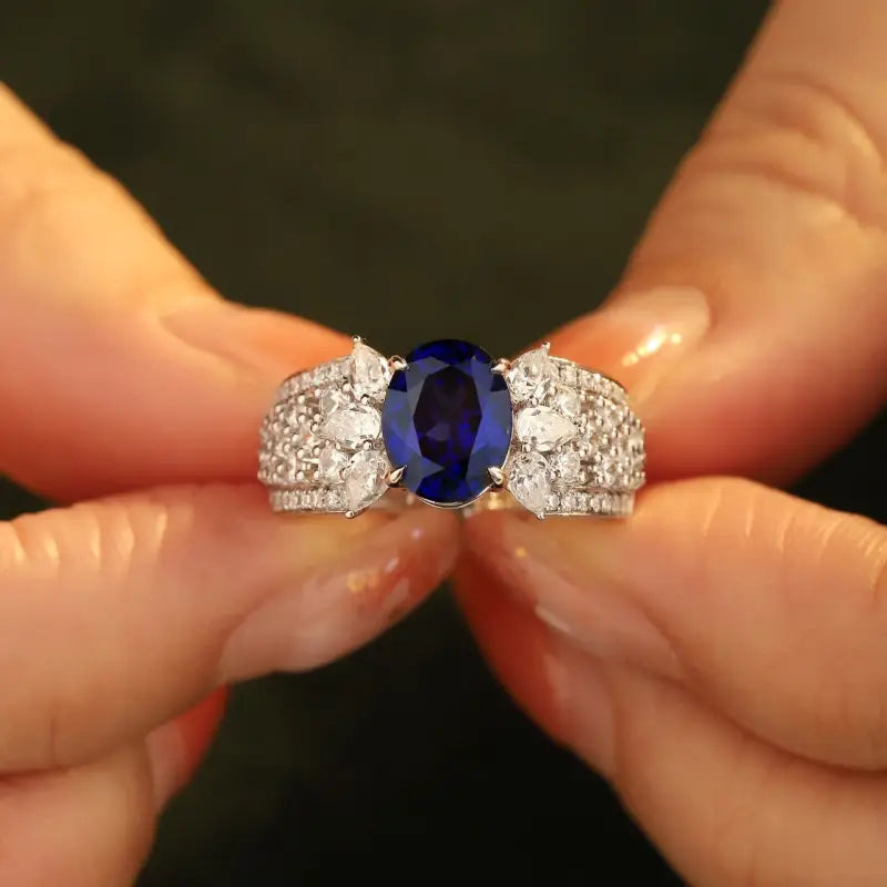 Ornate ring featuring a central oval blue gemstone flanked by diamonds.