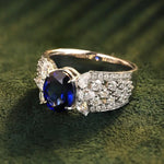 Load image into Gallery viewer, Elegant ring featuring a deep blue sapphire center stone surrounded by diamonds on a gold band.
