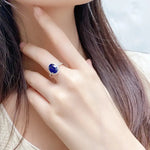 Load image into Gallery viewer, Sapphire ring with a diamond halo on a person’s finger.
