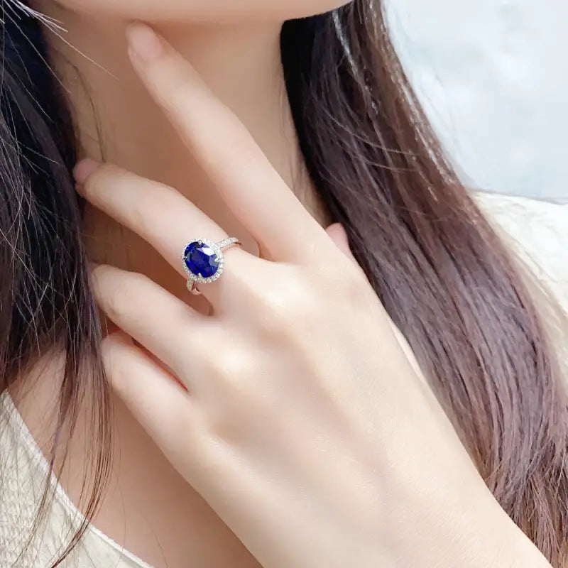 Sapphire ring with a diamond halo on a person’s finger.