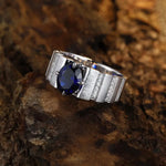 Load image into Gallery viewer, Silver ring with a prominent blue gemstone, likely a sapphire, set in a channel-style band.
