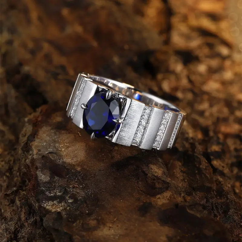 Silver ring with a prominent blue gemstone, likely a sapphire, set in a channel-style band.