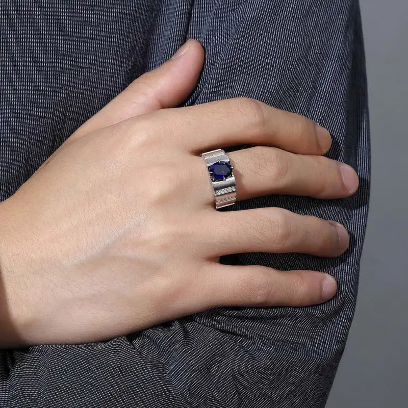 Silver ring with a dark blue gemstone worn on a person’s hand.