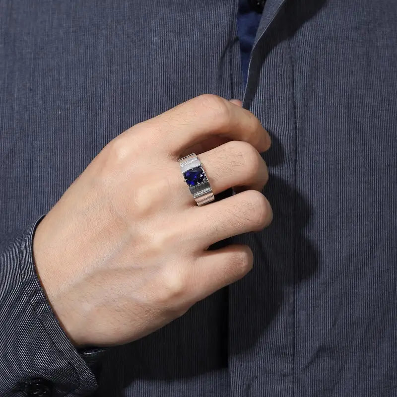 Ring with a square blue gemstone and silver band on a person’s finger.