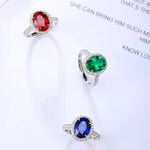 Load image into Gallery viewer, Three gemstone rings featuring red, green, and blue oval-cut stones surrounded by diamond halos.
