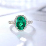 Load image into Gallery viewer, Emerald and diamond ring with an oval-cut green gemstone surrounded by small white diamonds set in a silver or white gold band.
