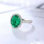 Load image into Gallery viewer, Emerald and diamond ring with an oval-cut green gemstone surrounded by small diamonds on a silver or white gold band.
