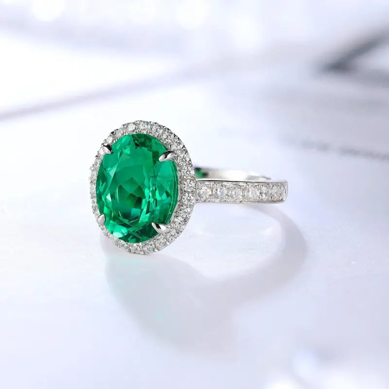 Emerald and diamond ring with an oval-cut green gemstone surrounded by small diamonds on a silver or white gold band.