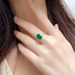 Load image into Gallery viewer, Emerald ring with a diamond-encrusted band on a person’s finger.
