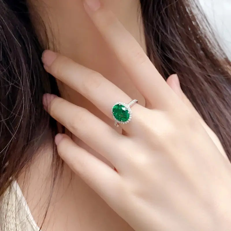 Emerald ring with a diamond-encrusted band on a person’s finger.