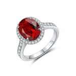 Load image into Gallery viewer, Oval-cut ruby ring with diamond halo and accented band set in white metal.
