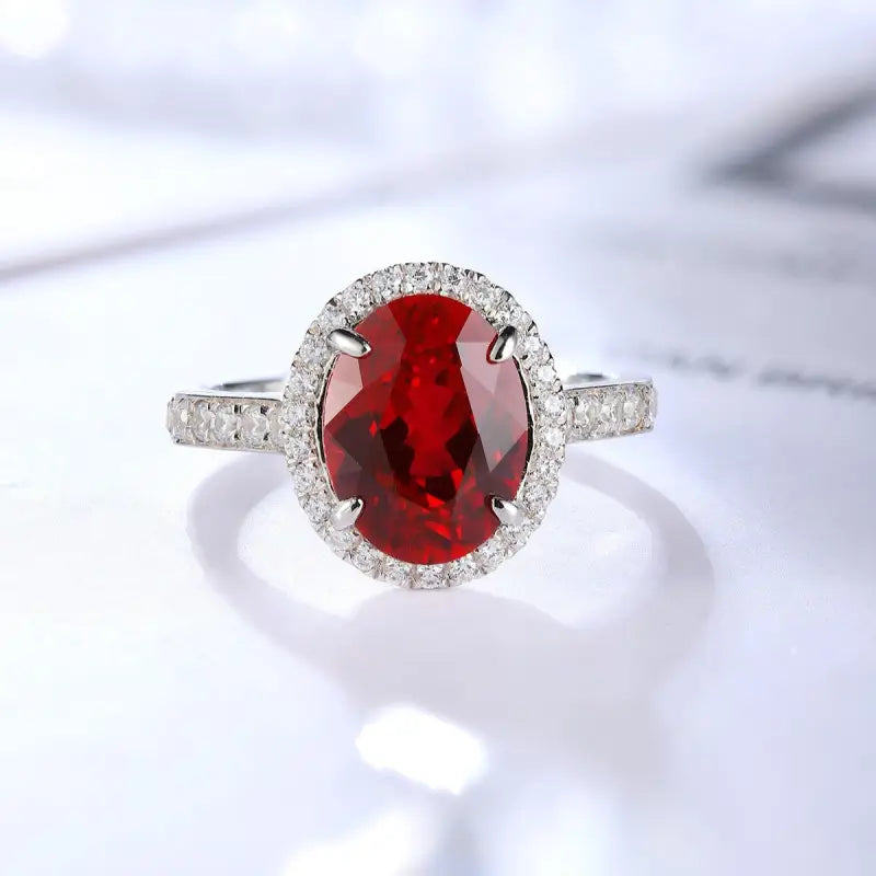 Oval-cut ruby ring with diamond halo and band set in white metal.