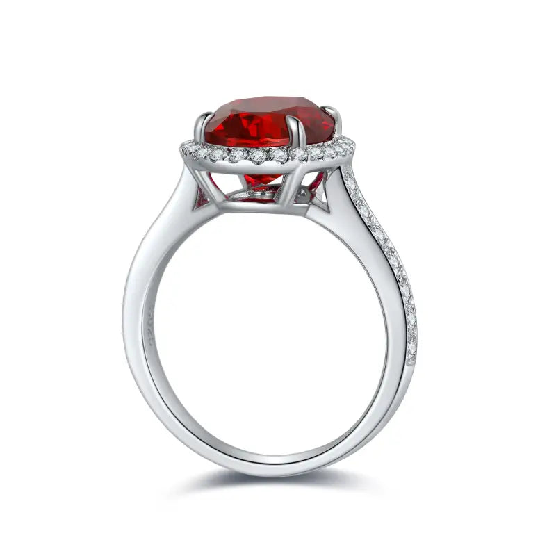 Silver ring with a prominent oval-cut red gemstone surrounded by small diamonds.