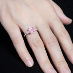 Load image into Gallery viewer, Pink diamond ring with white diamond accents on a finger.
