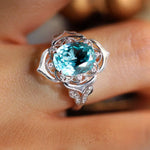 Load image into Gallery viewer, Ornate silver ring featuring a prominent oval-cut aquamarine gemstone surrounded by small diamonds.
