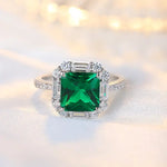 Load image into Gallery viewer, Emerald-cut green gemstone ring surrounded by diamonds in a white gold or platinum setting.
