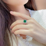 Load image into Gallery viewer, Emerald ring with diamond accents on a person’s finger.
