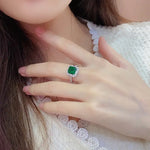 Load image into Gallery viewer, Emerald ring with a square-cut gemstone surrounded by smaller diamonds on a silver band.
