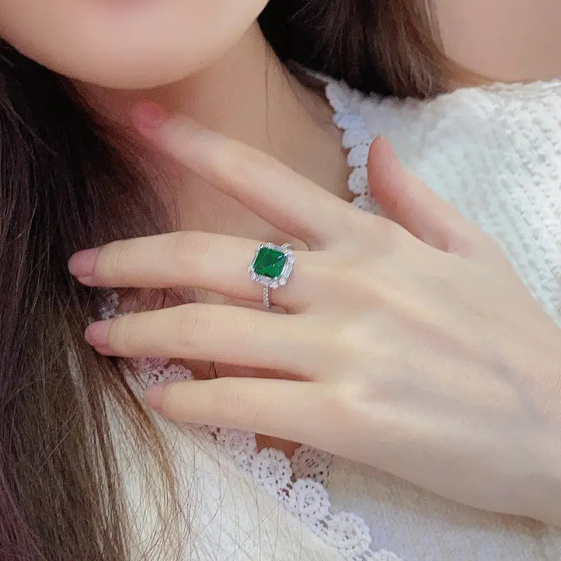 Emerald ring with a square-cut gemstone surrounded by smaller diamonds on a silver band.