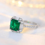 Load image into Gallery viewer, Emerald-cut green gemstone ring with diamond accents set in a white metal band.
