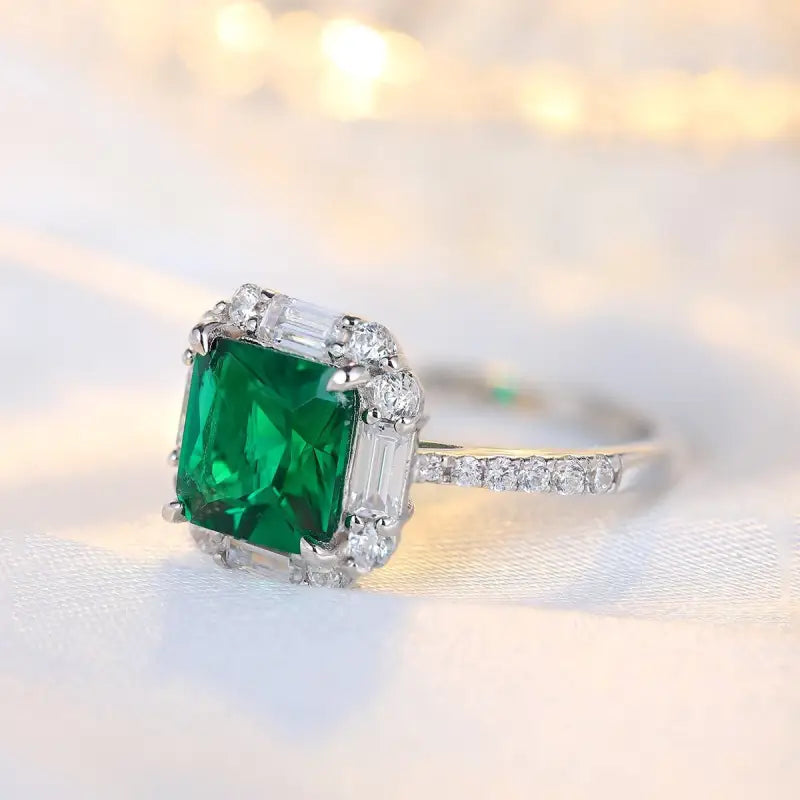 Emerald-cut green gemstone ring with diamond accents set in a white metal band.