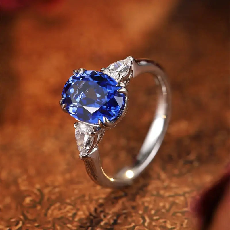 Elegant silver ring featuring a vibrant blue oval gemstone flanked by two smaller clear stones.