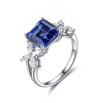 Load image into Gallery viewer, Silver ring featuring a square-cut blue gemstone flanked by clear crystal accents.
