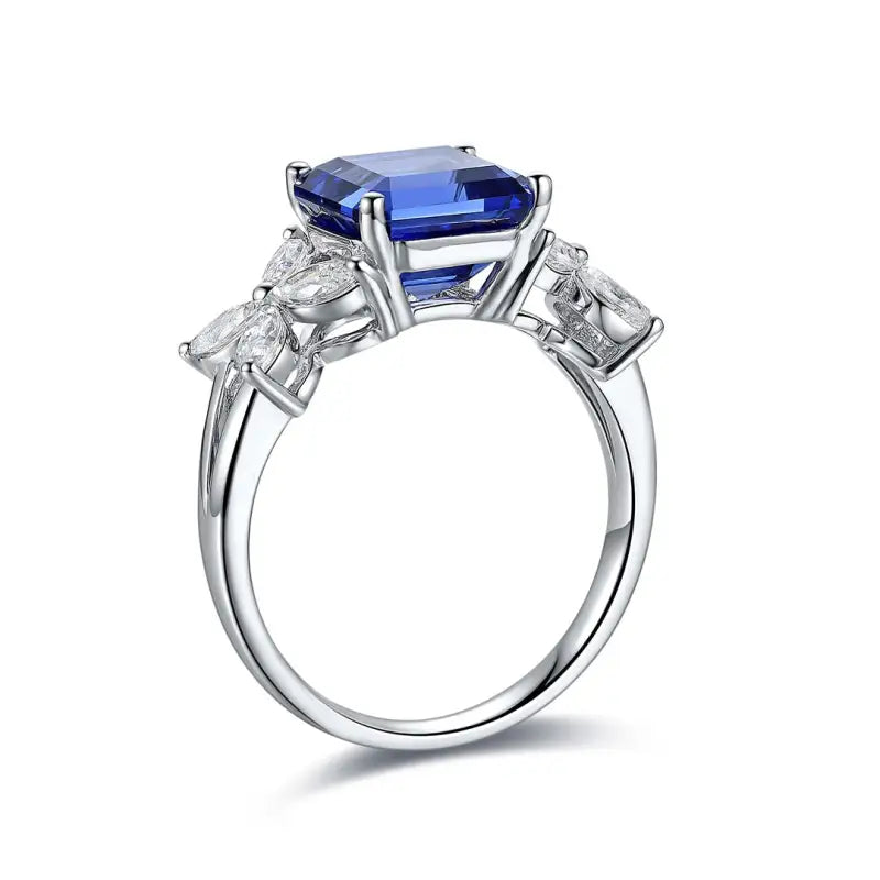 Elegant silver ring featuring a prominent blue gemstone flanked by clear diamonds.