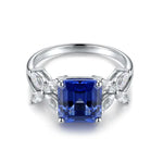 Load image into Gallery viewer, Silver ring featuring a square-cut blue sapphire gemstone flanked by smaller clear diamonds.
