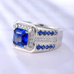 Load image into Gallery viewer, Silver ring featuring a square-cut blue sapphire centerpiece surrounded by smaller diamonds and sapphires.
