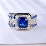 Load image into Gallery viewer, Ornate silver ring featuring a square-cut blue sapphire centerpiece surrounded by diamonds and smaller sapphires.
