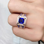 Load image into Gallery viewer, Ornate ring featuring a square-cut blue gemstone surrounded by smaller stones in a silver or white gold setting.
