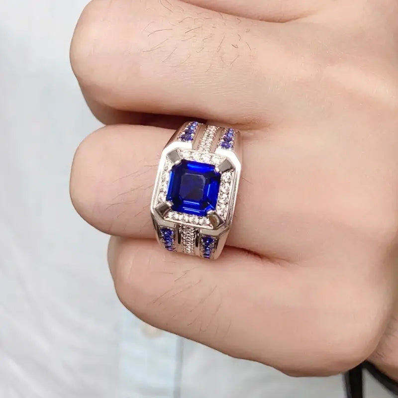 Ornate ring featuring a square-cut blue gemstone surrounded by smaller stones in a silver or white gold setting.