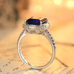 Load image into Gallery viewer, Elegant silver ring featuring a deep blue gemstone surrounded by smaller clear stones.
