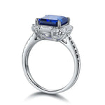 Load image into Gallery viewer, Silver ring featuring a prominent rectangular blue gemstone surrounded by smaller clear stones.
