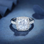 Load image into Gallery viewer, Diamond engagement ring with a cushion-cut center stone surrounded by a halo of smaller diamonds on a pave band.
