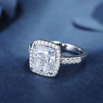 Load image into Gallery viewer, Diamond engagement ring with a cushion-cut center stone surrounded by a halo of smaller diamonds on a pave band.
