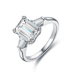 Load image into Gallery viewer, Diamond engagement ring with an emerald-cut center stone and tapered baguette side stones set in a white metal band.
