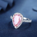 Load image into Gallery viewer, Pear-shaped pink gemstone ring with diamond halo and silver band.
