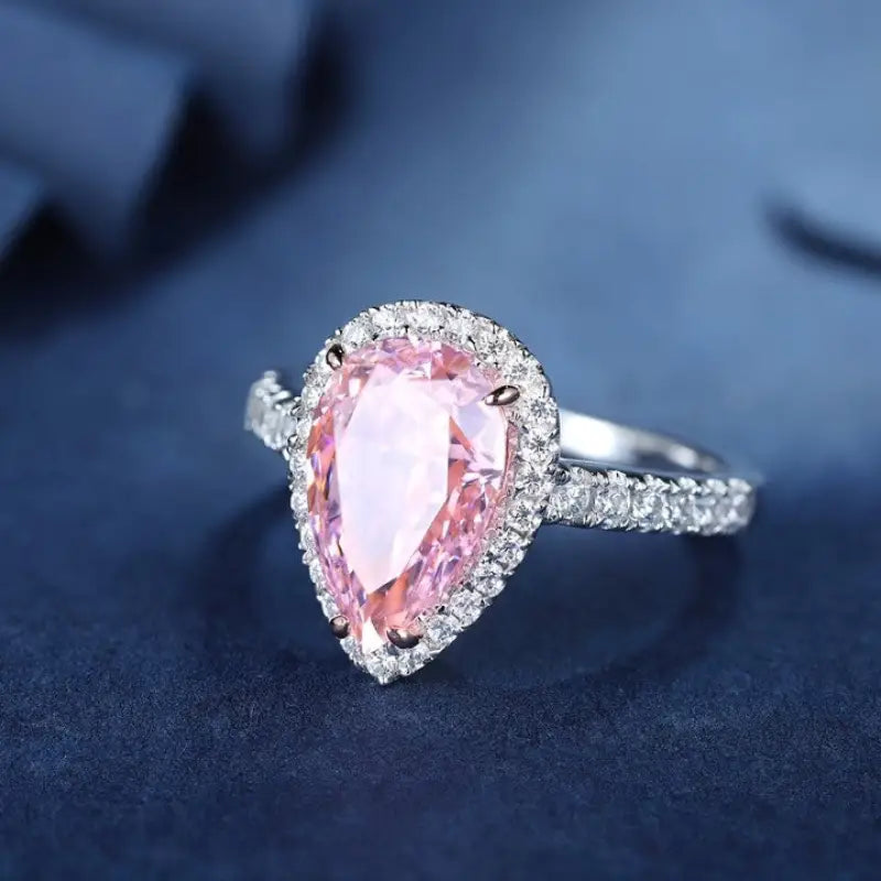 Pear-shaped pink gemstone ring with diamond halo and silver band.