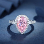 Load image into Gallery viewer, Pear-shaped pink diamond ring with a halo of smaller white diamonds on a silver band.
